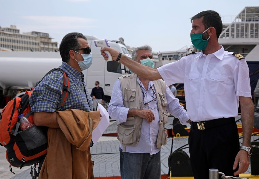 A crew member checks a man's temperature before boarding a ferry in Piraeus. Greece has resumed travel from the mainland to islands. REUTERS.